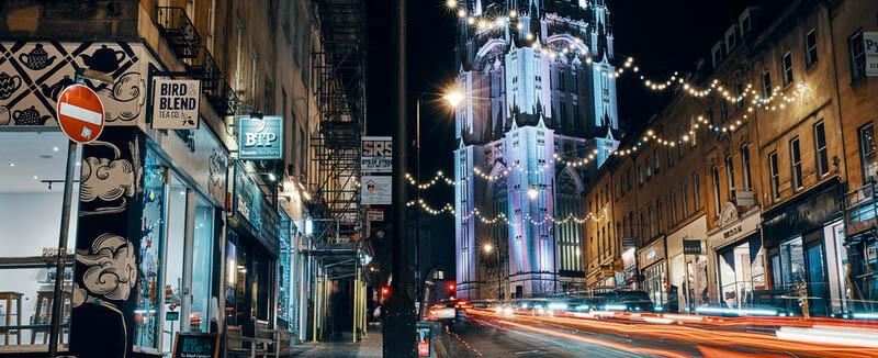 a photo looking up park street towards the wills memorial building taken at night. some of the lights in the image are blurred.